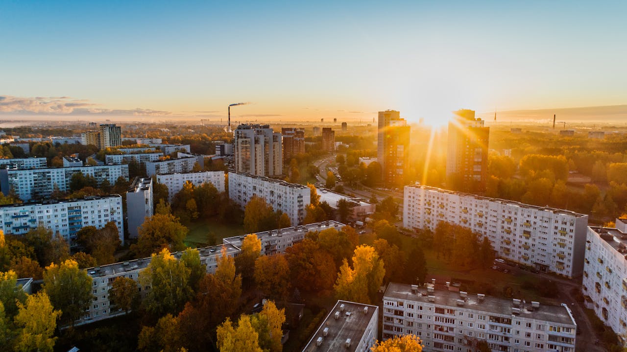 Aerial view of a cityscape at sunrise with autumn foliage and modern buildings.